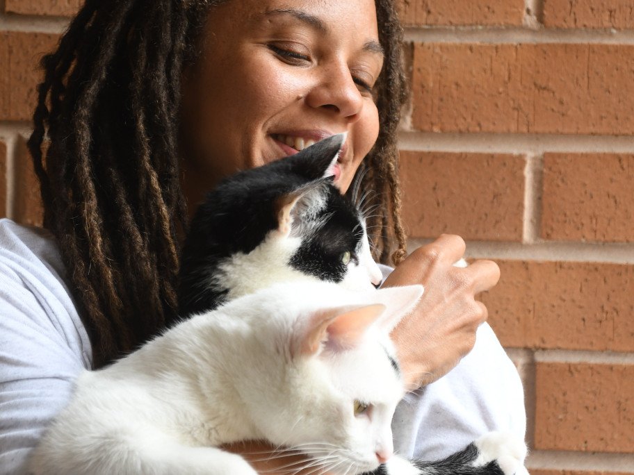 A woman gently cradles a cat in her arms as they both gaze out of a window